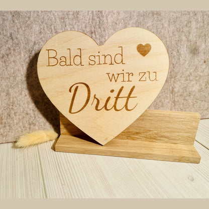 Herz aus Holz mit der aufschrift "Bald sind wir zu dritt" zum Scchwangerschaft mitteilen Schild Das Glückswerk