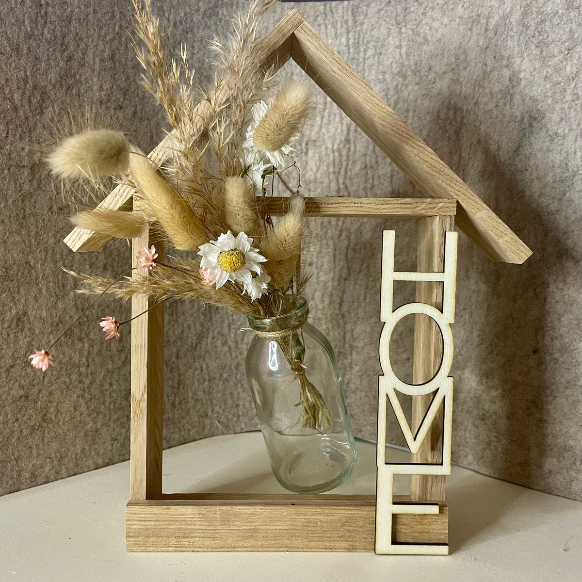 Holzhaus mit Glasvase und Trockenblumen und Aufschrift Home Dekoration Das Glückswerk
