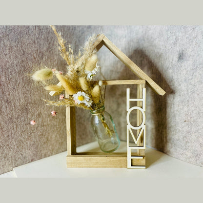 Holzhaus mit Glasvase und Trockenblumen und Aufschrift Home Dekoration Das Glückswerk