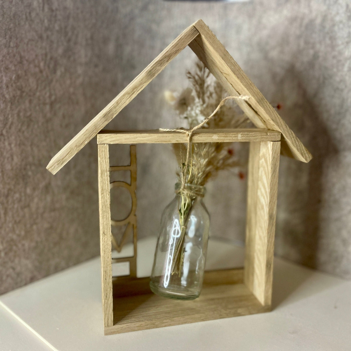 Holzhaus mit Glasvase und Trockenblumen und Aufschrift Home Dekoration Das Glückswerk