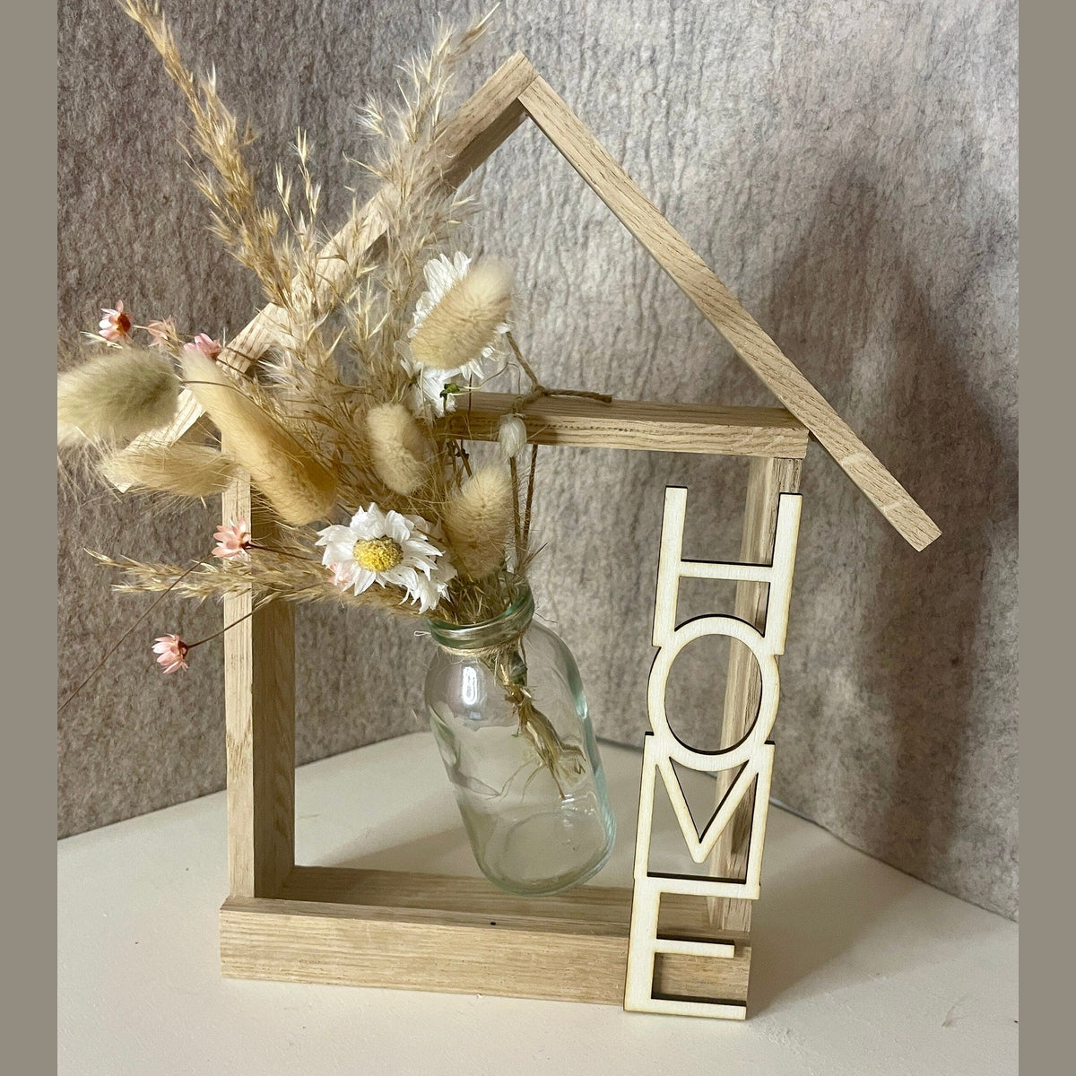 Holzhaus mit Glasvase und Trockenblumen und Aufschrift Home Dekoration Das Glückswerk