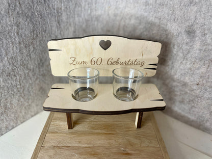 Holzbank mit Gravur „Zum 60. Geburtstag“ und zwei leeren Gläsern
