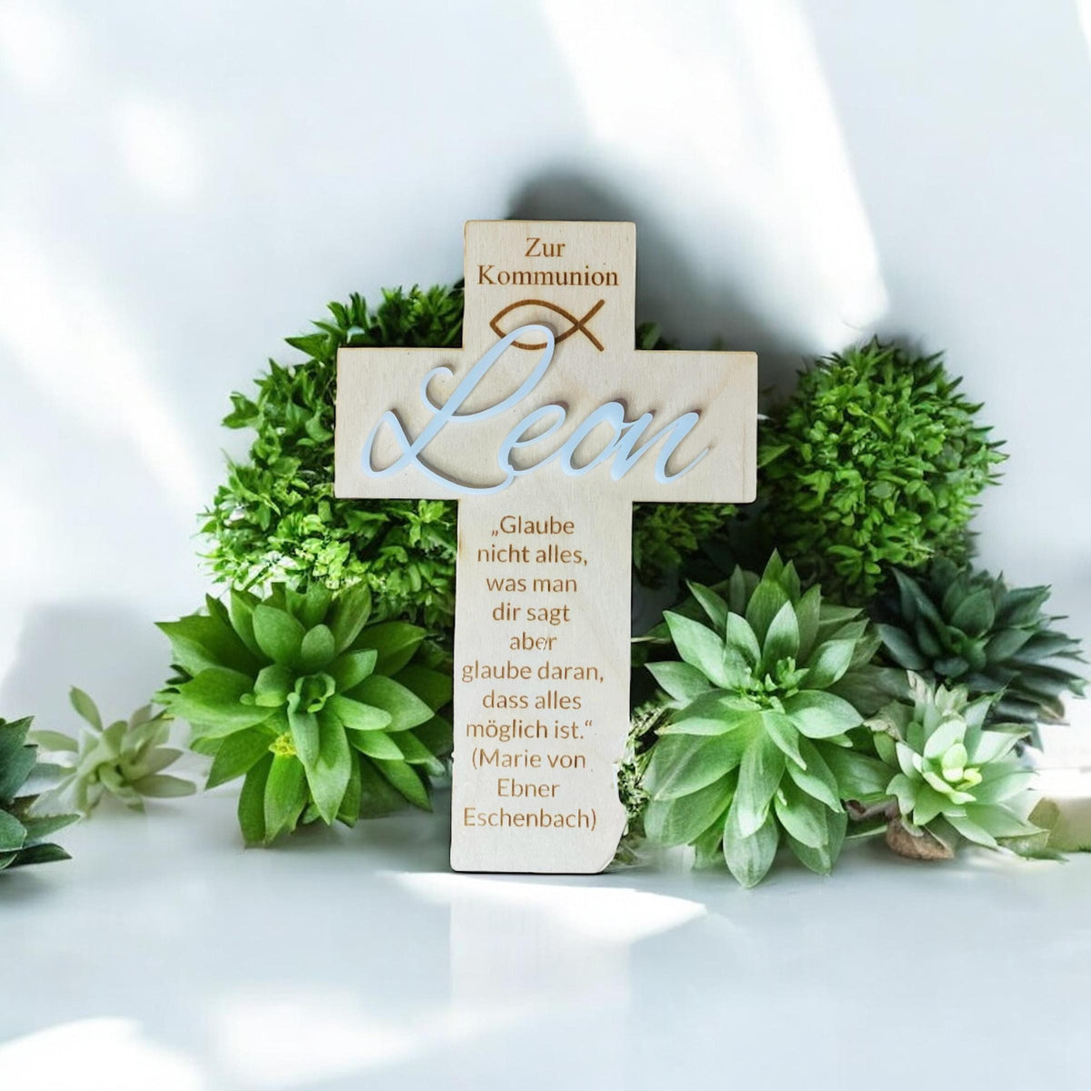 Taufkreuz mit Acrylglas-Namensschild „Leon“ vor grünen Pflanzen