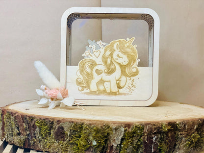 Holzspardose mit Einhorn-Motiv auf moosbewachsenem Holzstumpf